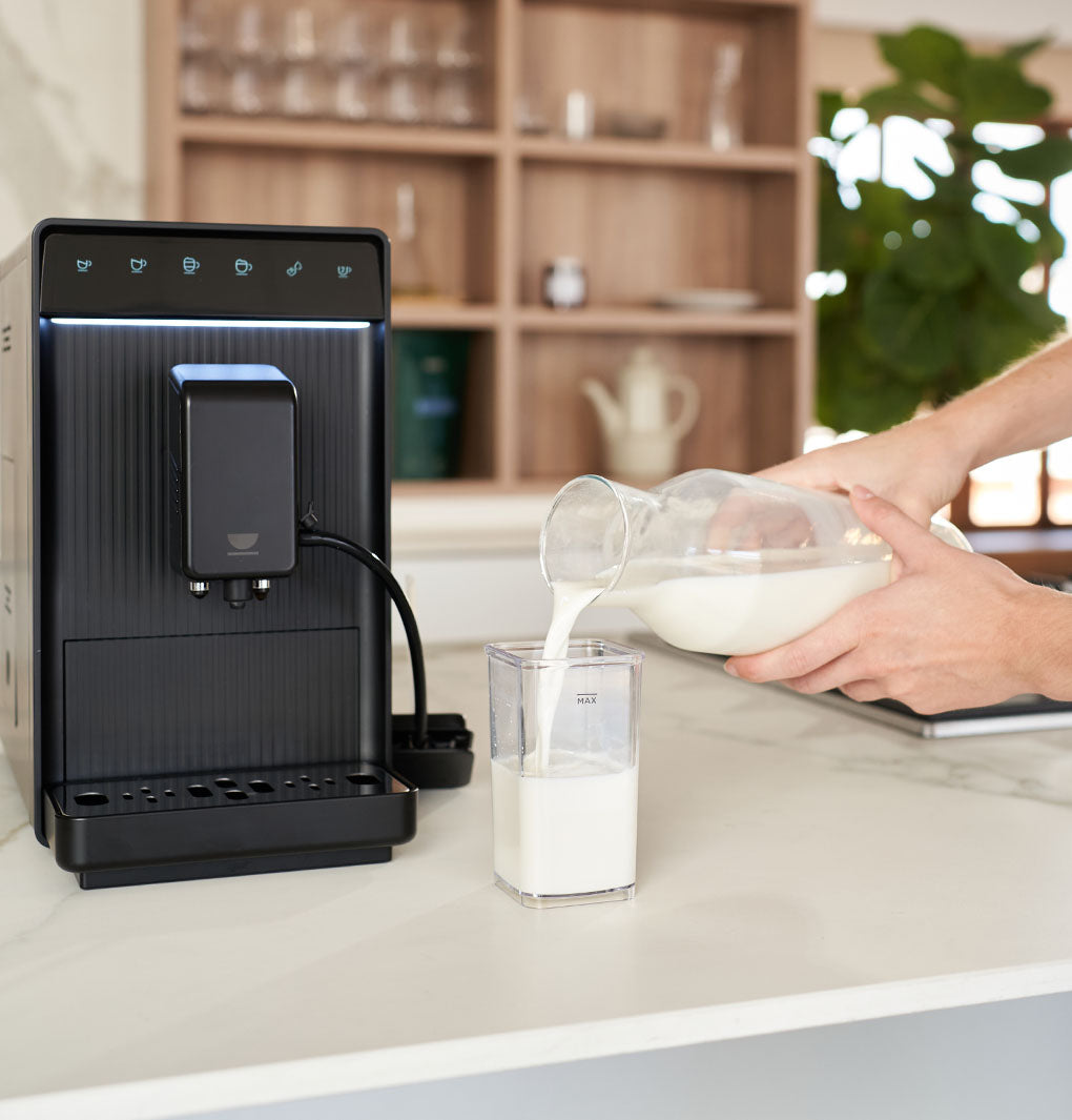 Le mani riempiono il serbatoio del latte della caffettiera INCAPTO Aura Milk sul bancone della cucina