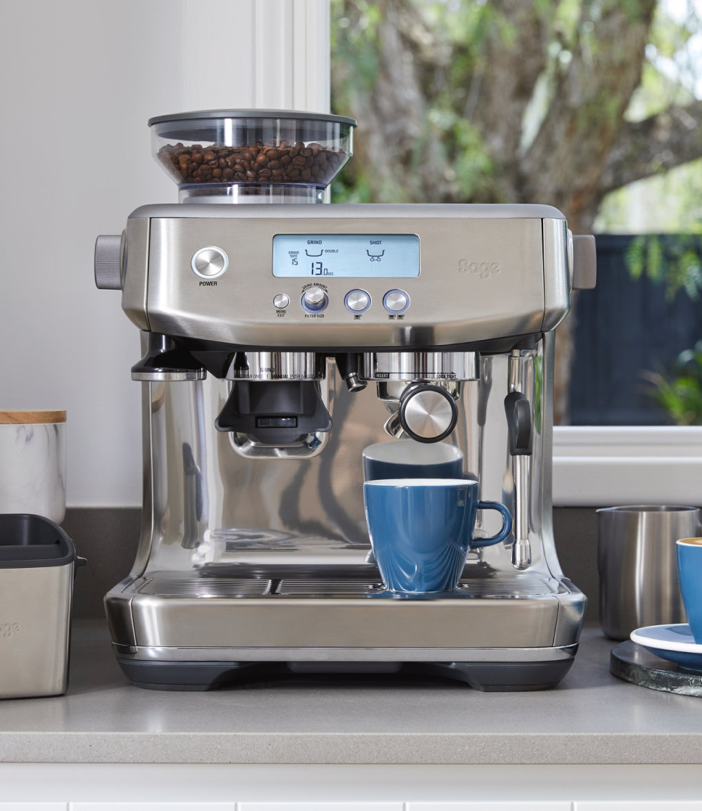 Cafetera a taulell de cuina amb tassa de cafè i dos cafès preparats
