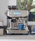 Cafetera a taulell de cuina amb tassa de cafè i dos cafès preparats
