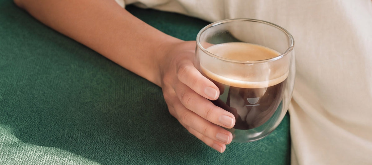 Una mano sostiene un vaso de café de especialidad recién hecho sobre un sofá verde