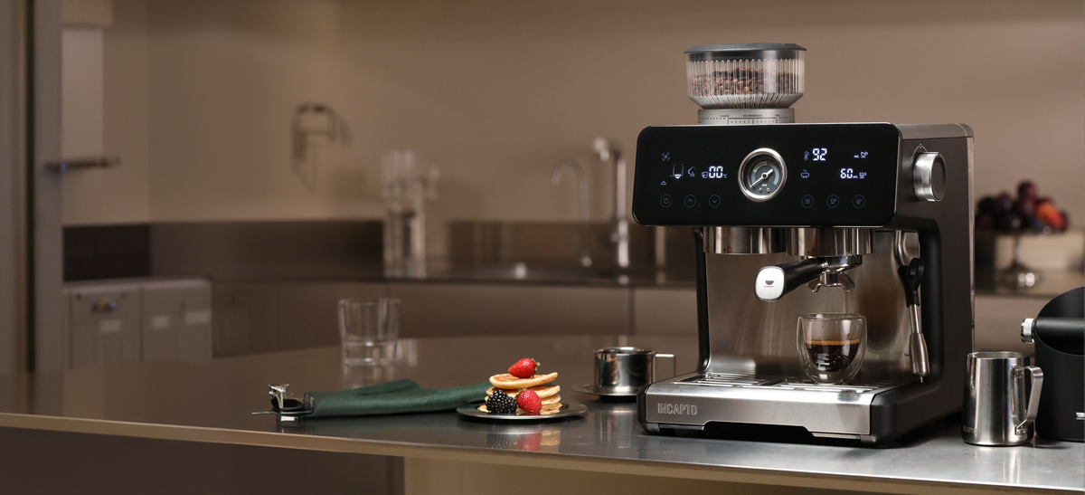 Cafetera INCAPTO Sabi sobre la encimera de una cocina, junto a una jarra de leche y un knock box