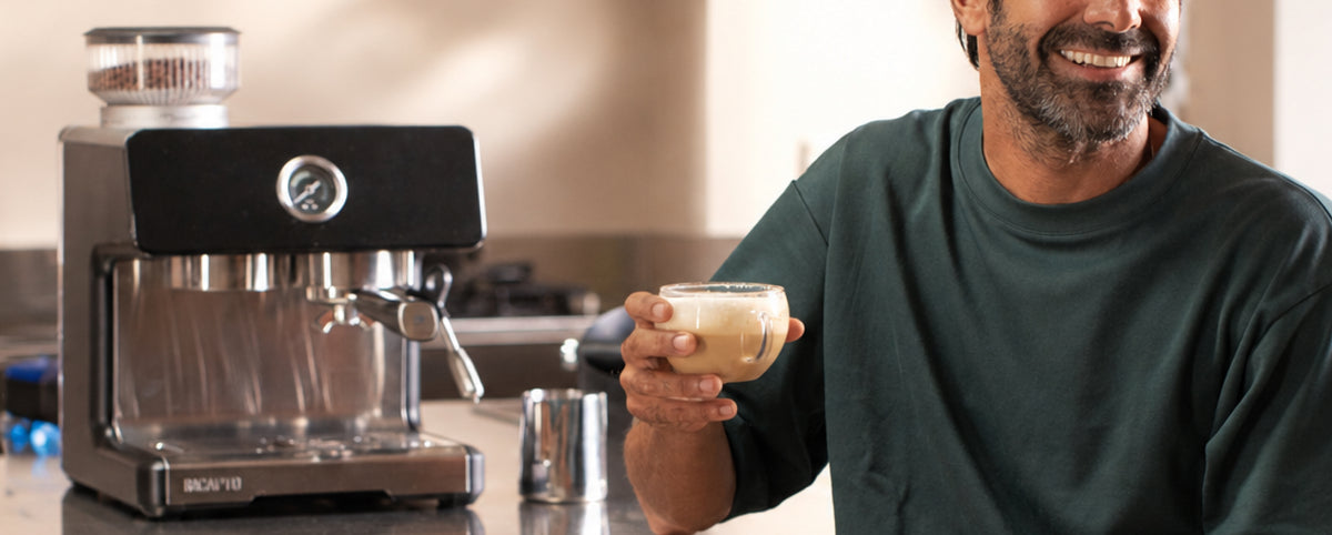 Hombre sonriendo con un café con leche junto a la cafetera INCAPTO Sabi