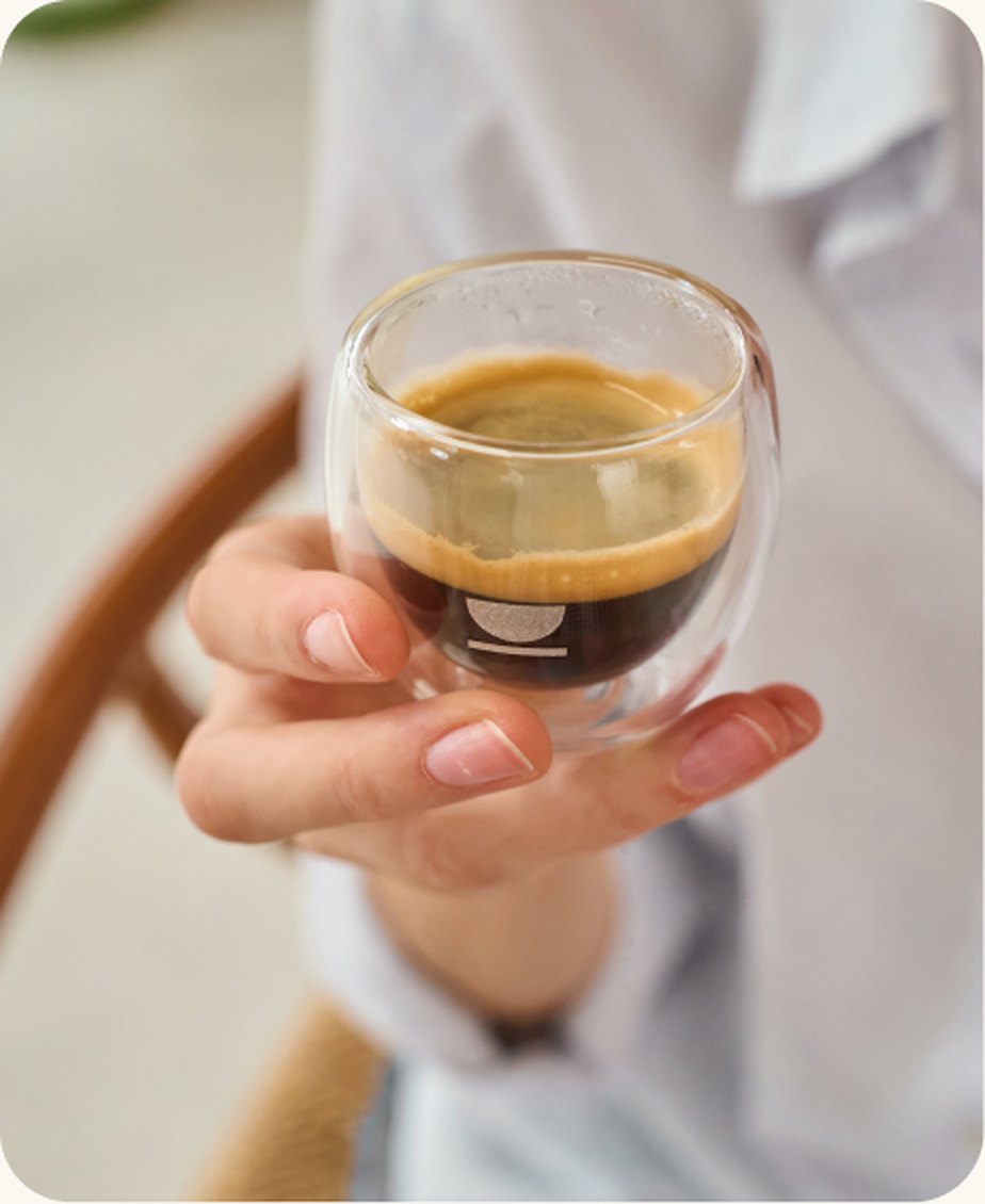 Una mano sostiene un espresso de café de especialidad en un vaso de doble cristal