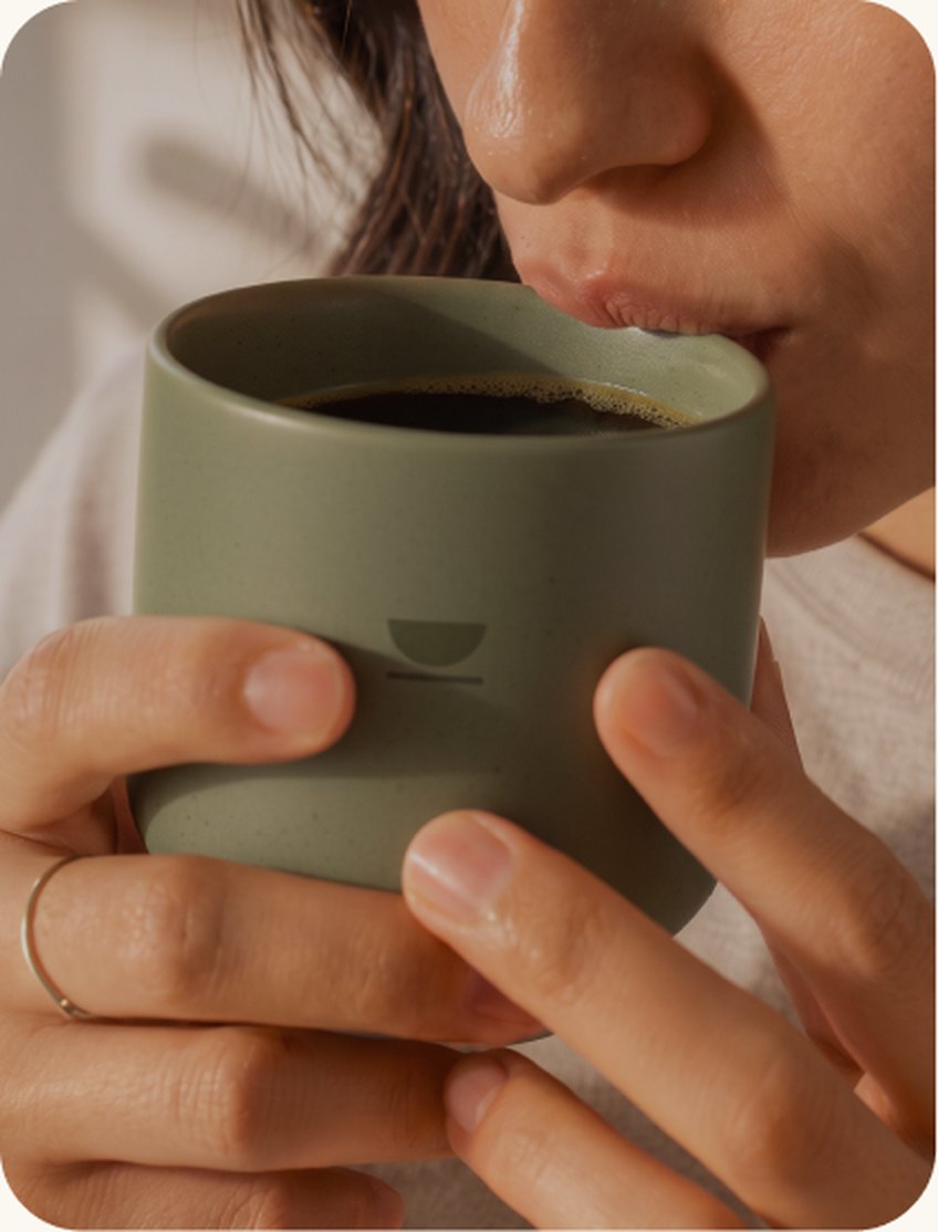 Mujer bebiendo café de especialidad en una taza de cerámica verde