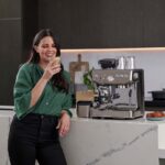 Une fille dans une cuisine avec un café late à la main et une machine à café sage barista express impress.