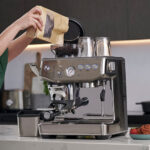 Personne versant du café en grain dans la trémie d'une cafetière semi-automatique Sage Barista Express Impress