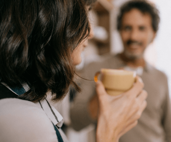 Una mujer sostiene una taza de café mientras conversa con un hombre en un ambiente hogareño y relajado.