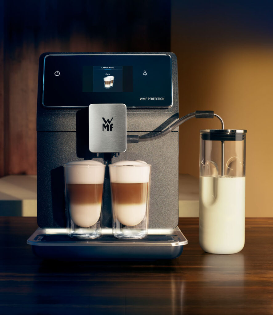 Macchina da caffè WMF Perfection 860L su piano di legno con due tazze di latte macchiato e serbatoio del latte